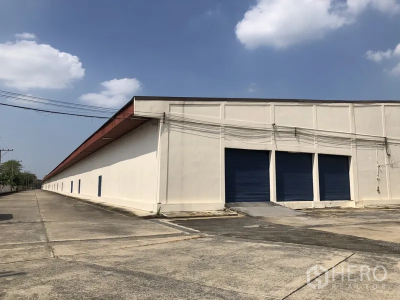 货栈 出租在Lam Luk Ka, Pathum Thani - 仓库侧立面，配多扇蓝色卷闸装卸门与坡道
