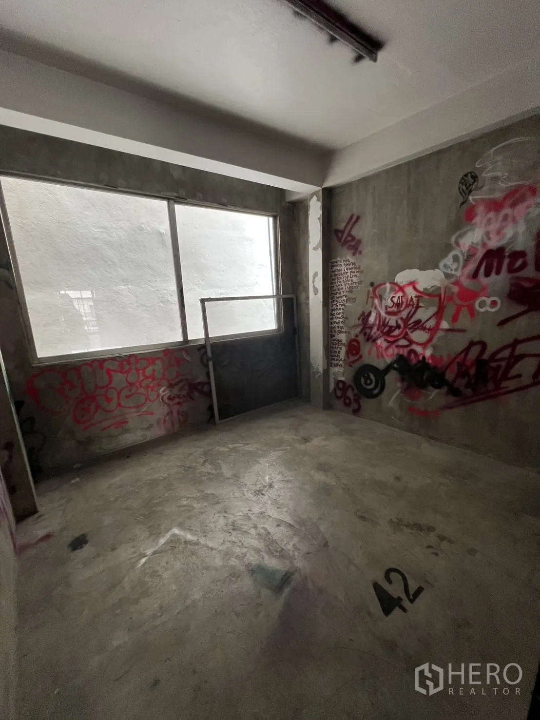 Shophouse for rent in Watthana, Bangkok - Unfinished room with graffiti on raw concrete walls and large window.