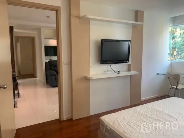 Condominium for rent or sale in Khlong Toei, Bangkok - Bedroom with wall-mounted TV, wood flooring, and a window with greenery outside.