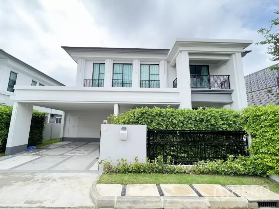 Detached House for rent in Khan Na Yao, Bangkok - Front view of a modern two-storey corner detached house with covered 2-car carport, black gate and manicured hedge.