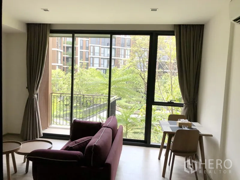 Condominium for rent in Watthana, Bangkok - Living area with sofa and dining nook opening to a balcony with green courtyard view.