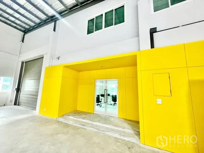 Warehouse for sale in Lam Luk Ka, Pathum Thani - Bright yellow office entrance with glass doors and mezzanine inside the warehouse hall.