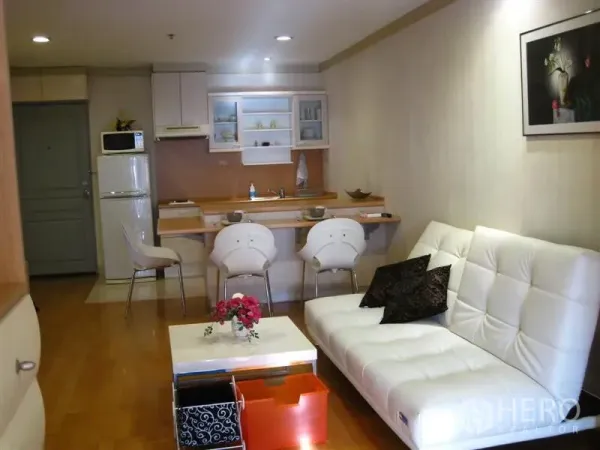 公寓 出租在Khlong Toei, Bangkok - 开放式起居区，白色沙发、木地板，配备吧台的小厨房。