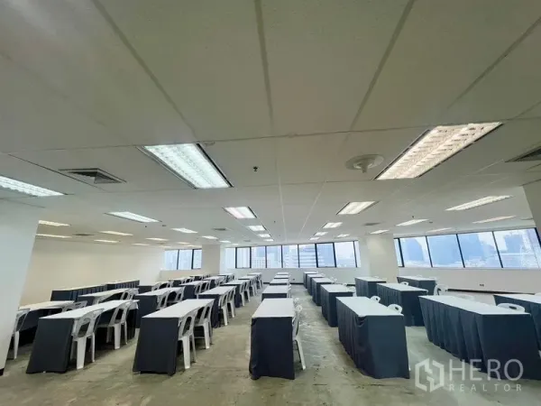 Office Space for rent - Classroom-style layout under grid ceiling with fluorescent lighting and wide windows across the wall.