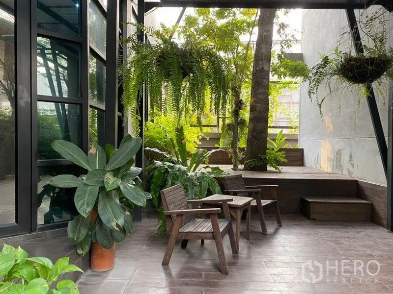 办公空间 出租在Bang Kapi, Bangkok - 绿意庭院露台，吊兰与盆栽，木椅靠建筑外墙。