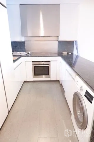 Condominium for sale in Sathon, Bangkok - Modern U-shaped kitchen with stone counters, oven, cooktop, and washer.