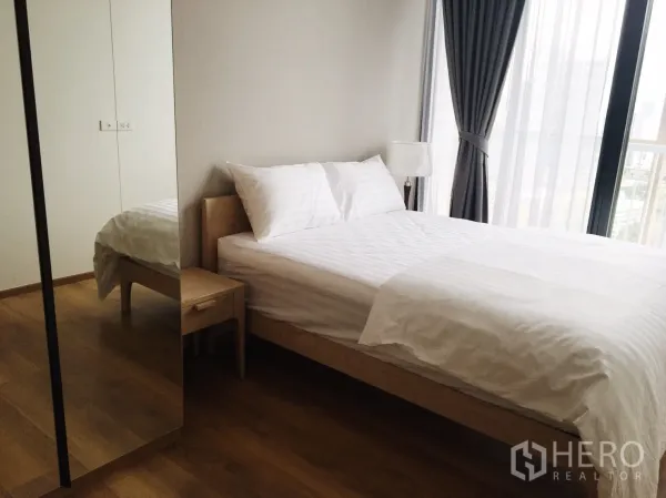 Condominium for rent in Khlong Toei, Bangkok - Bright bedroom with wood floors, mirrored wardrobe and floor-to-ceiling windows with city view.
