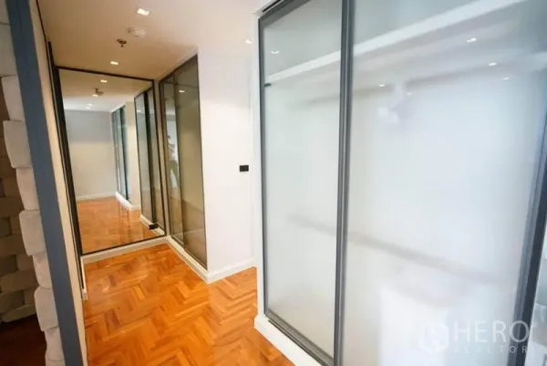 Condominium for rent or sale in Bang Na, Bangkok - Bright corridor with frosted glass wardrobes, mirrored doors and herringbone wood flooring.