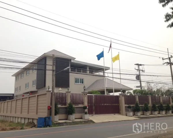 Factory for sale in Khlong Luang, Pathum Thani - Corner exterior of the factory compound with perimeter wall, gate, and flagpoles.