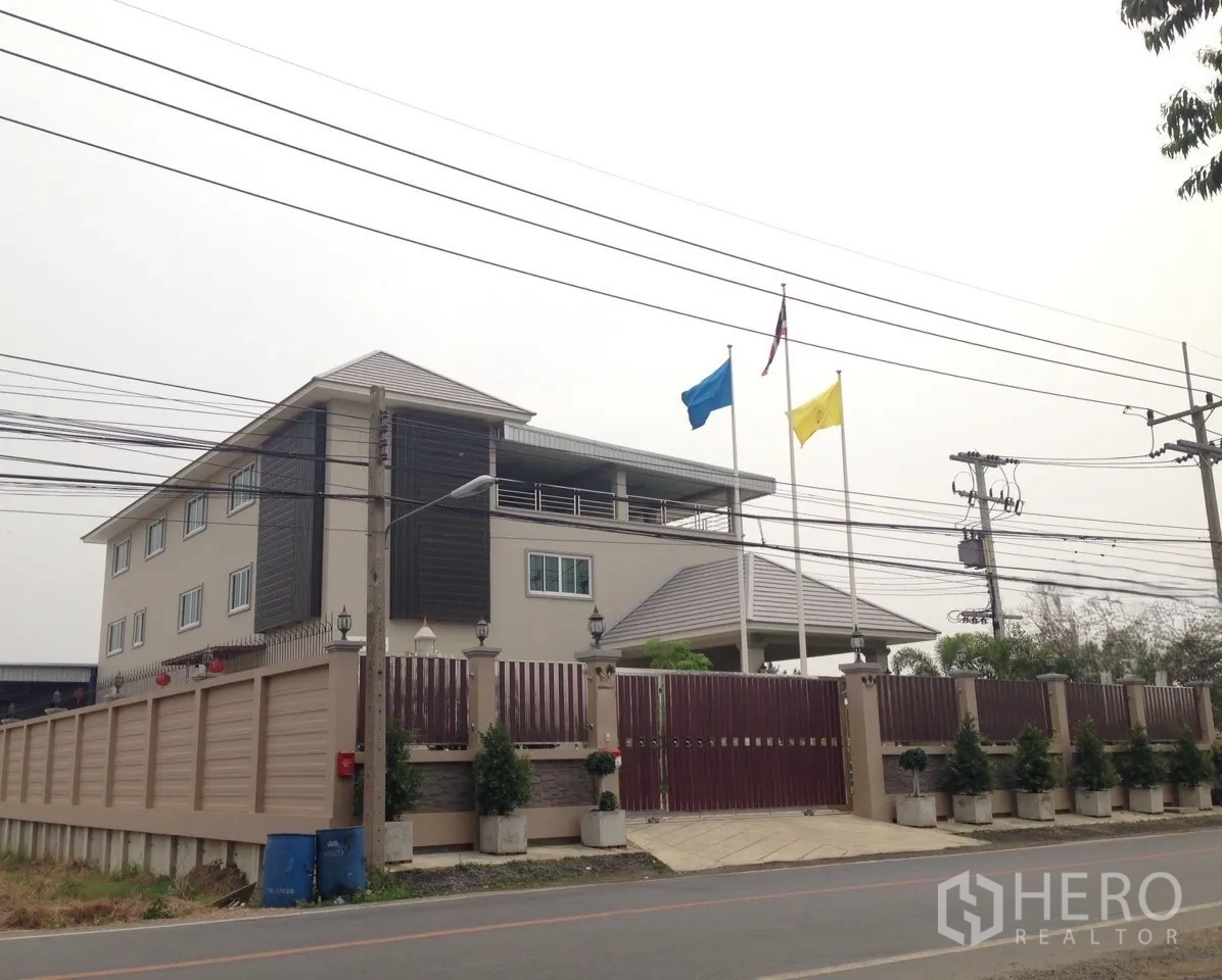 Factory for sale in Khlong Luang, Pathum Thani - Corner exterior of the factory compound with perimeter wall, gate, and flagpoles.