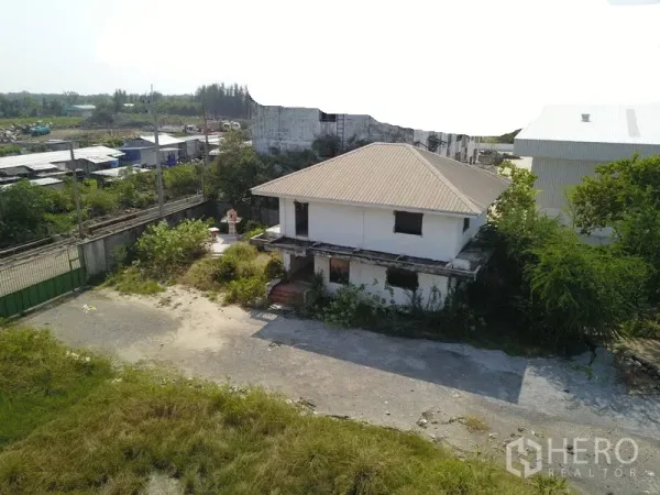 Factory for sale in Samut Prakan - Two-storey site office/house inside the industrial compound with driveway and trees.