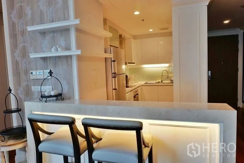 Condominium for rent in Khlong Toei, Bangkok - Cozy breakfast bar with two stools beside display shelves leading to a bright white kitchenette.