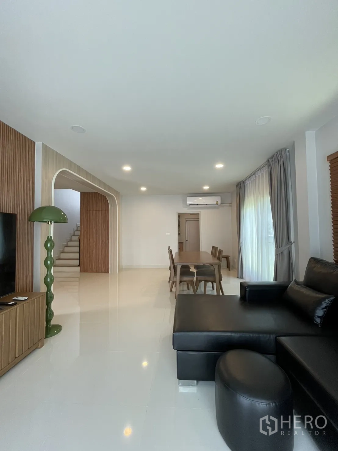 独立式住宅 出租在Bang Phli, Samut Prakan - 开放式客餐厅，黑色皮沙发、木餐桌与明亮窗帘。