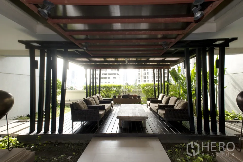 Condominium for rent in Sathon, Bangkok - Shaded outdoor lounge pavilion with wooden deck, rattan sofas and greenery at a Sathon condominium.