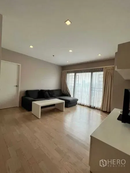 Condominium for rent in Khlong Toei, Bangkok - Minimalist living space with sectional sofa, coffee table and sheer curtains.