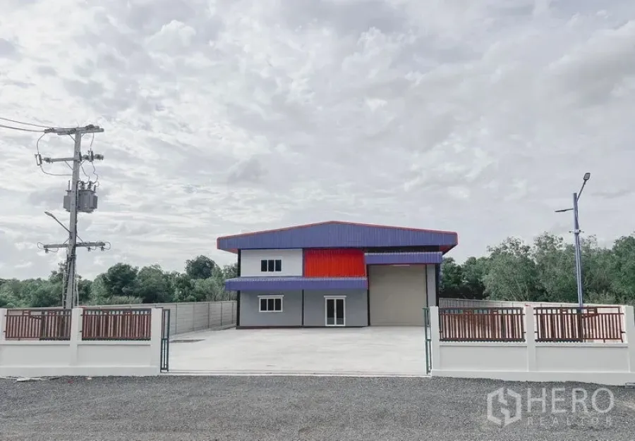 货栈 出租或出售在Khlong Luang, Pathum Thani - 现代仓库正面，带大门与宽阔混凝土前院及两层办公区，周围绿树。