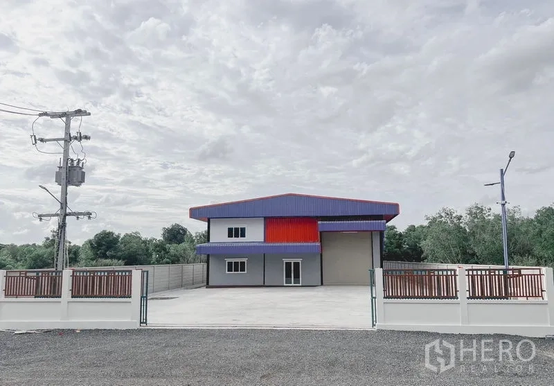 货栈 出租或出售在Khlong Luang, Pathum Thani - 现代仓库正面，带大门与宽阔混凝土前院及两层办公区，周围绿树。