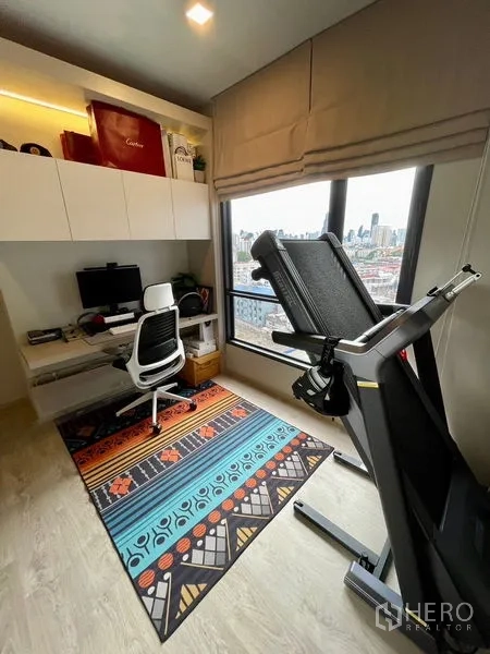 Condominium for sale - Work-from-home room with desk, treadmill and wide window overlooking Bangkok skyline.