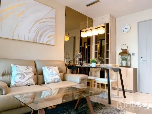 Condominium for rent in Watthana, Bangkok - Contemporary living room with beige sofa, glass coffee table and a dining area under pendant lights.