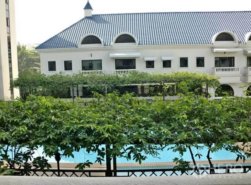Townhouse for rent in Khlong Toei, Bangkok - View of communal swimming pool and clubhouse with blue roof framed by greenery.