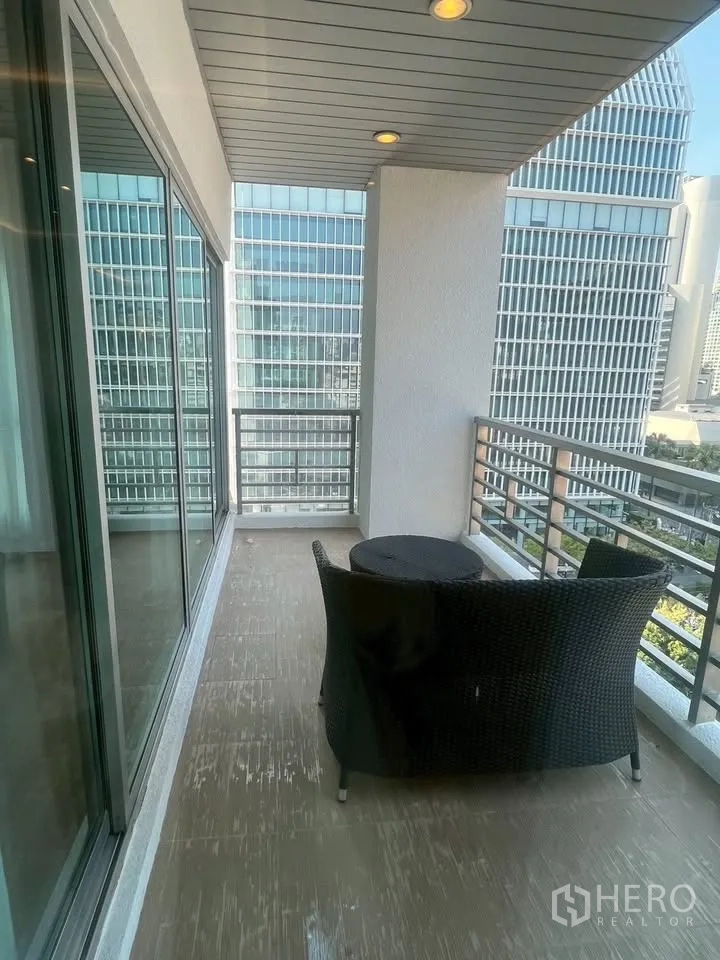 公寓 for rent in Pathum Wan, Bangkok - 宽敞阳台配藤椅与小桌，推拉玻璃门与筒灯，可眺望高楼城市景观。