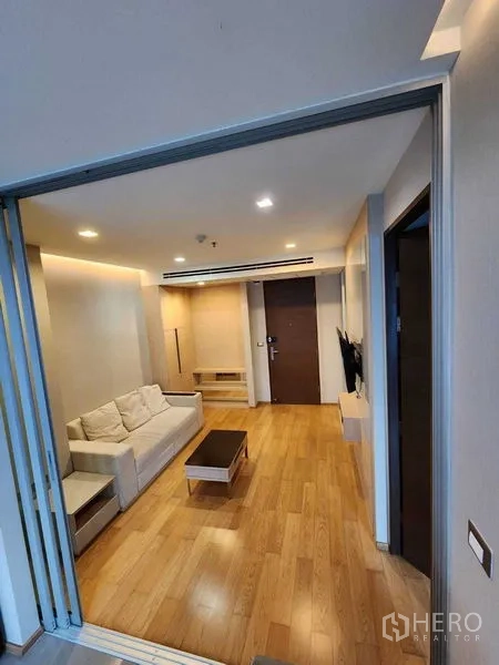 公寓 出售在Ratchathewi, Bangkok - 起居室配沙发、壁挂电视与茶几，木地板与嵌灯营造舒适氛围。