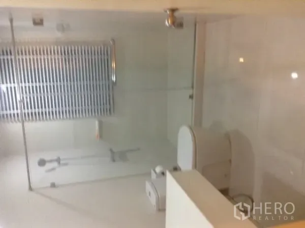 Condominium for rent or sale in Din Daeng, Bangkok - Second bathroom with a toilet and large glass shower enclosure in neutral tones.