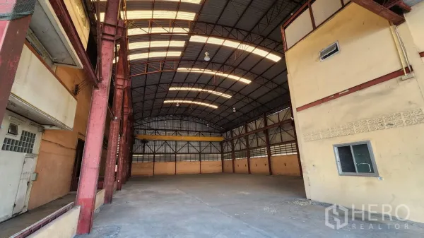 Warehouse for rent in Nonthaburi - Spacious warehouse interior with high arched roof, skylights, and red steel columns.