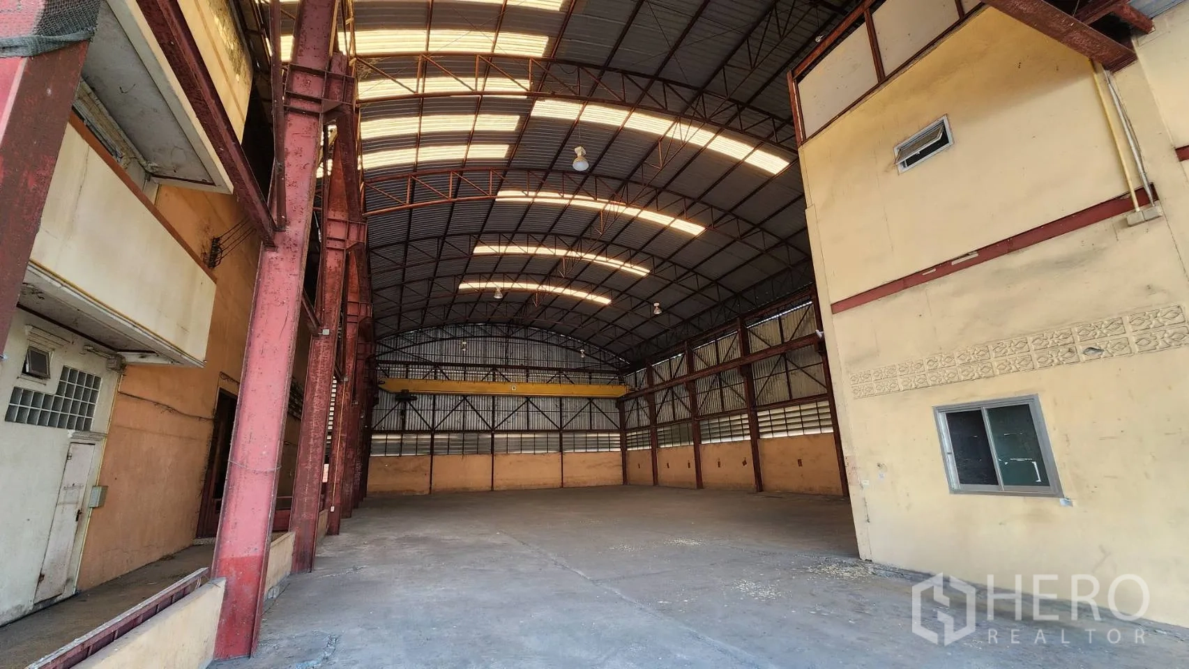 Warehouse for rent in Nonthaburi - Spacious warehouse interior with high arched roof, skylights, and red steel columns.