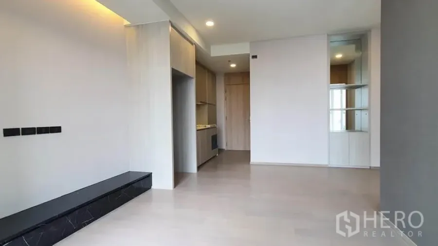 Condominium for sale in Khlong Toei, Bangkok - Bright open-plan living area with light wood floors, built-in TV ledge and kitchenette in a modern condo.