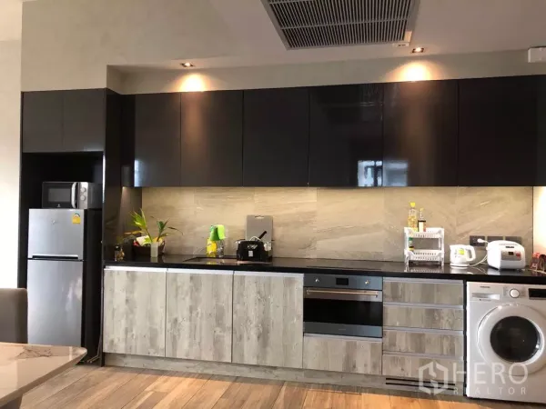 Condominium for sale in Watthana, Bangkok - Modern linear kitchen with glossy black and wood cabinets, built-in hob and oven, refrigerator, and washing machine.