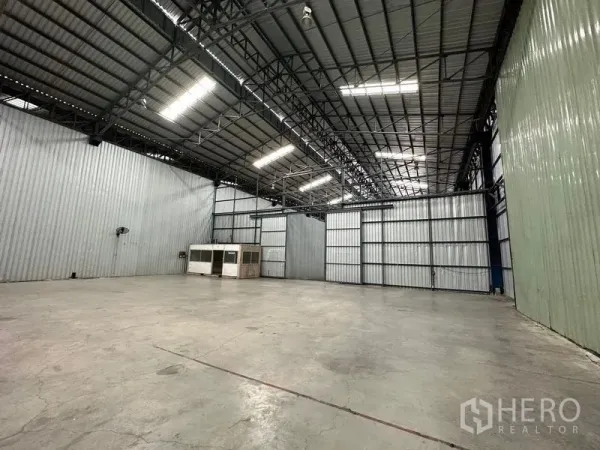 Warehouse for rent in Pak Kret, Nonthaburi - Warehouse hall showing steel framework, large sliding metal doors and expansive floor area.