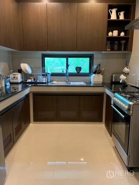 Detached House for rent or sale in Bang Kapi, Bangkok - U-shaped kitchen with wood cabinets, stone countertops, window and gas stove.