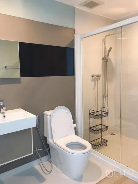 Condominium for rent in Bang Rak, Bangkok - Clean bathroom with glass shower enclosure, toilet and wall-mounted sink.