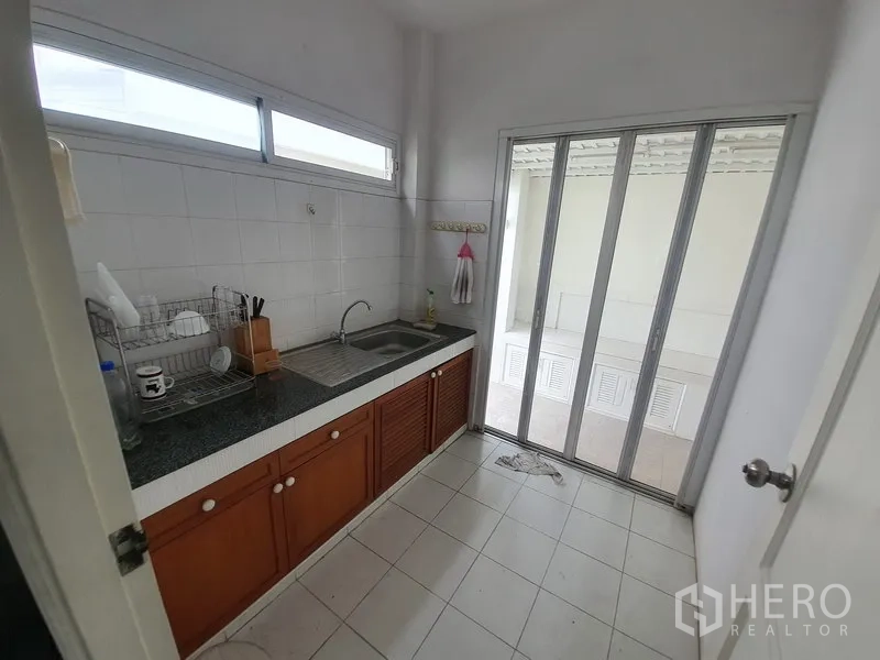 独立式住宅 出租在Lat Krabang, Bangkok - 独立泰式厨房，双槽水池、白色瓷砖墙，推拉玻璃门通向工作阳台。