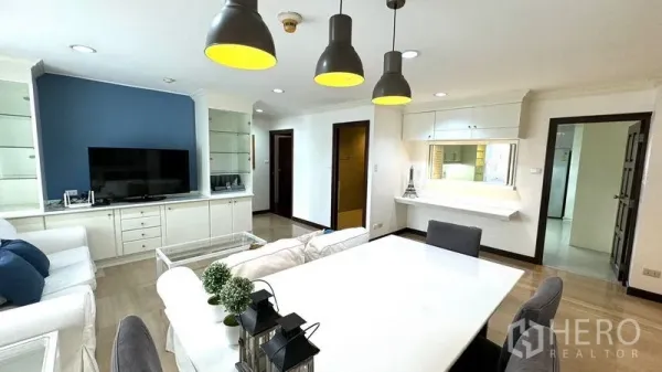 Condominium for rent or sale in Watthana, Bangkok - Open-plan living and dining area with white sofas, TV wall unit, and black pendant lights.