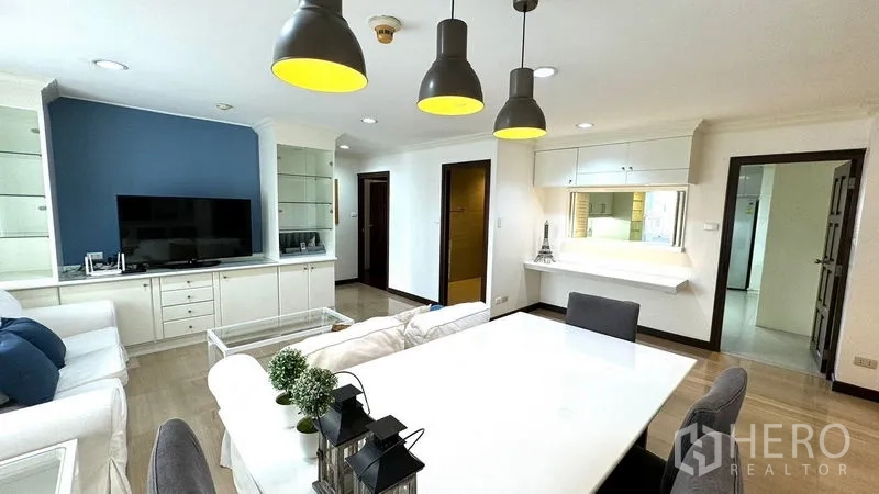Condominium for rent or sale in Watthana, Bangkok - Open-plan living and dining area with white sofas, TV wall unit, and black pendant lights.