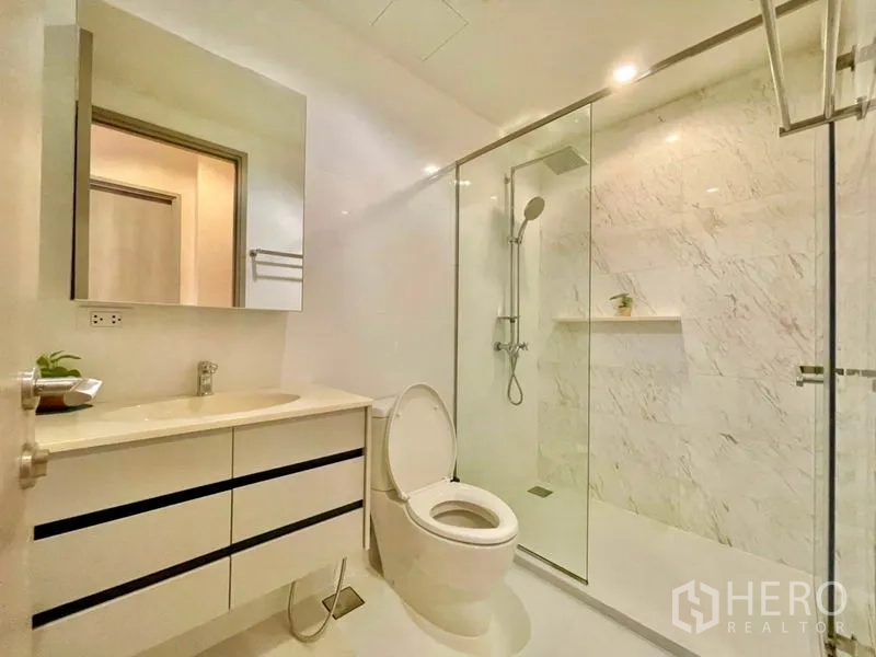 Condominium for rent or sale in Watthana, Bangkok - Modern bathroom with vanity, toilet and glass‑enclosed rain shower.
