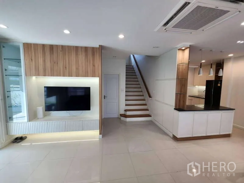 独立式住宅 出租在Sathon, Bangkok - 明亮起居区，电视墙、楼梯与厨房岛台一览。