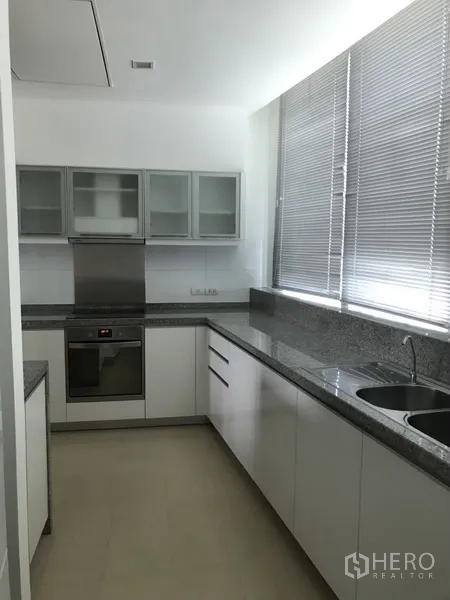 Condominium for rent in Khlong Toei, Bangkok - Separate kitchen featuring white cabinetry, granite countertops, stainless oven and double sink with large window.