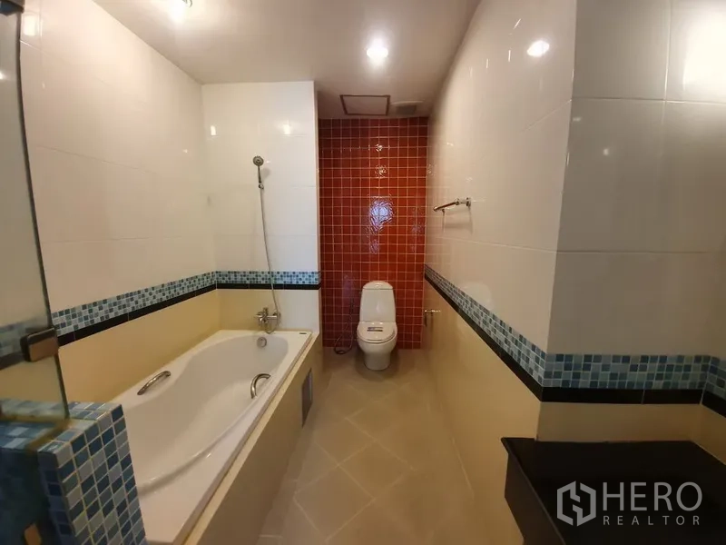 Condominium for rent in Khlong Toei, Bangkok - Wide view of bathroom featuring long bathtub and red tiled accent wall.