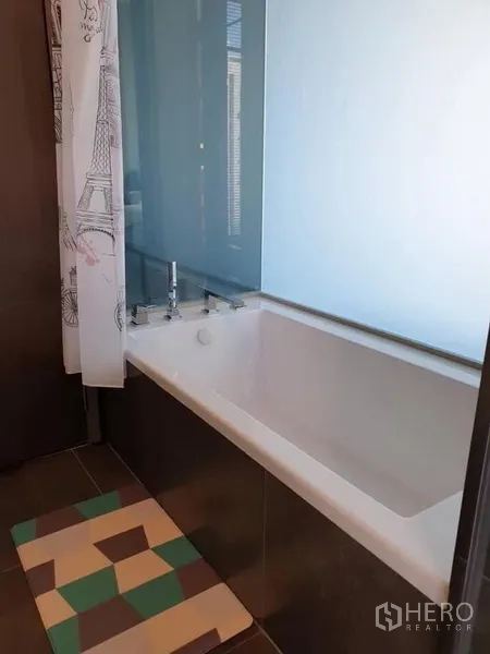 คอนโด ให้เช่าในHuai Khwang, Bangkok - มุมอ่างอาบน้ำสีขาว พร้อมฉากกั้นกระจกฝ้าและพรมเช็ดเท้าลายเรขาคณิต