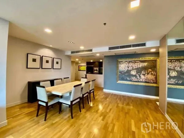 Condominium for rent or sale in Sathon, Bangkok - Dining area facing a semi-open kitchen with wall art and recessed lighting.