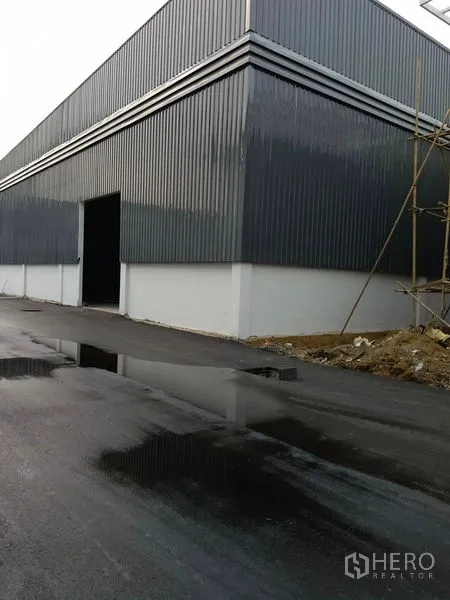 Warehouse for rent in Khlong Toei, Bangkok - Corner view of a warehouse with an open loading door beside a wet asphalt access road.