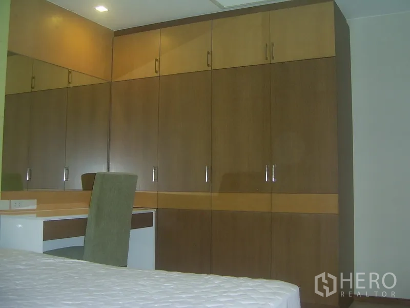 Condominium for rent in Khlong Toei, Bangkok - Wall of built-in wardrobes with a dressing table and chair in the bedroom.