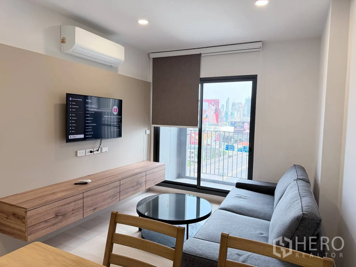 公寓 for rent in Din Daeng, Bangkok - 客厅配壁挂电视、空调和通向阳台的推拉门，可见城市景观。
