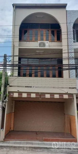 Shophouse for rent in Phra Khanong, Bangkok - Three-story shophouse facade with roll-up shutter and arched balcony above the storefront.