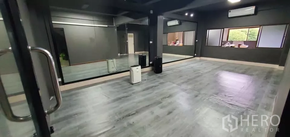 Office Space for rent in Suan Luang, Bangkok - Studio room with large wall mirror, dark wood-look floor, split air conditioners and windows.