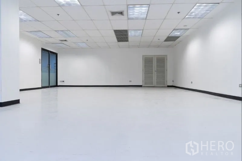 办公空间 出租在Ratchathewi, Bangkok - 宽敞白色办公室，格栅吊顶带空调出风口，侧面玻璃入口门与设备柜。