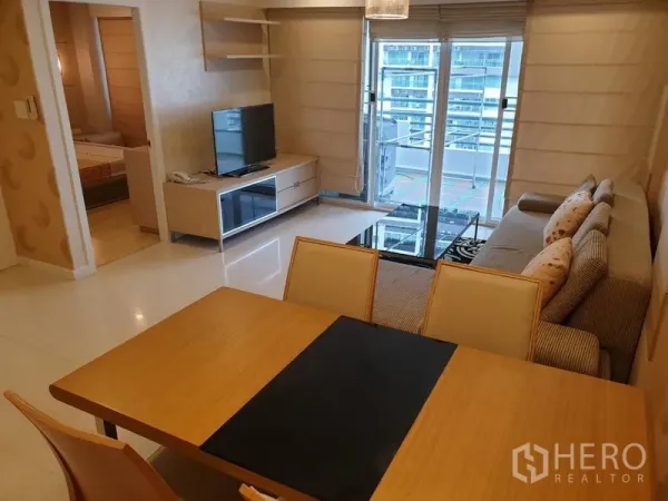 公寓 出租在Watthana, Bangkok - 明亮客餐厅，沙发与电视柜，落地玻璃门通向阳台，可见城市景观。